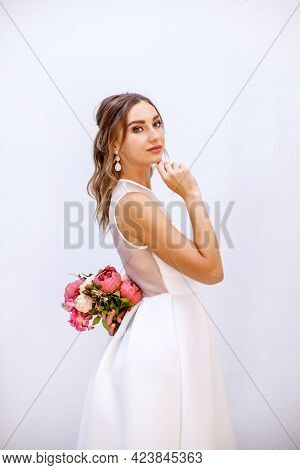 Brunette Girl In A Wedding Dress. Bride In A White Dress With A Bouquet In Her Hands. Makeup.