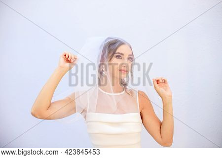 A Brunette Girl In A Wedding Dress Covers Her Face With A Veil. Bride In A White Dress. Makeup.