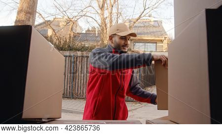 Delivery Man Wearing Cap And Red Uniform Lifting Cardboard Boxes. Stack Of Parcel Boxes. Concept Of 