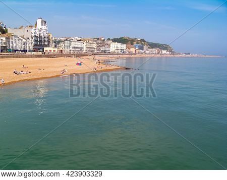 A view of a sunny beach with a town line, a few beachgoers and a calm emerald sea