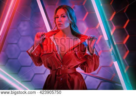 Stylish sexy woman in trendy red jacket posing in the light of neon lamps. Techno style, disco. Fashion shot.