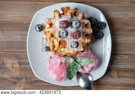Belgian waffles with strawberry ice cream, fresh raspberries and mint over wooden table. Flat lay. Top view.