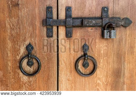 Close-up Of Wooden Doors With Wrought Iron Handles And A Deadbolt.
