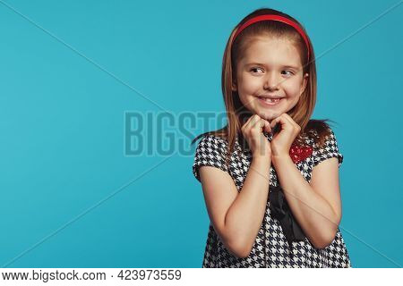 Delighted Girl Looking On Right Freespace, Smiling And Gesturing Heart
