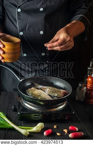 Professional Chef Prepares Fresh Fish In Pan Sprinkling Salt With The Ingredients. Preparing To Cook