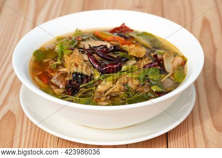 Sour And Spicy Smoked Dry Fish Soup In A White Ceramic Plate On A Wooden Table . Tom Klong In Thai. 