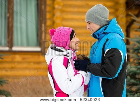 Half-length portrait of embracing couple looking at each other who wears warm caps and jackets during winter holidays