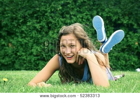 Smiling teenager laying down in a grass in a park