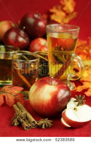 Apple surround by cinamone stick, anise, cup with apple juice and a basket with red apple in background