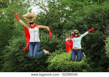 Super team of super hero girl with red cape, red gloves and black mask jumping in the air