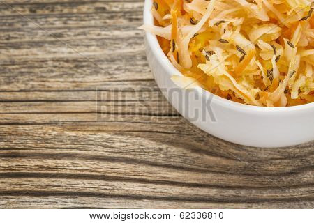 sauerkraut salad with carrot, caraway seeds and olive oil - a small bowl against grained wood
