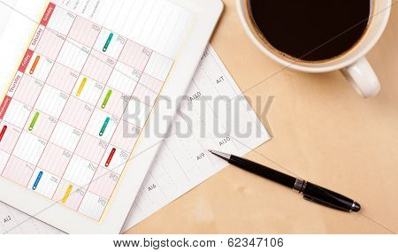 Workplace with tablet pc showing calendar and a cup of coffee on a wooden work table close-up