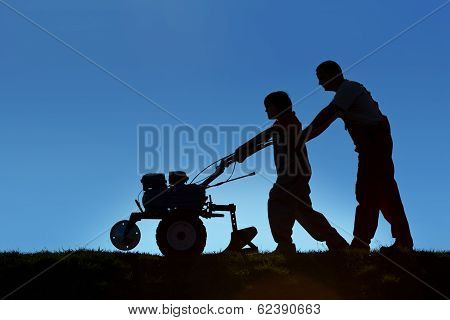 Father And Son Working The Land With A Tiller
