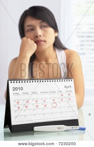 Mulher triste com teste de gravidez negativo e calendário