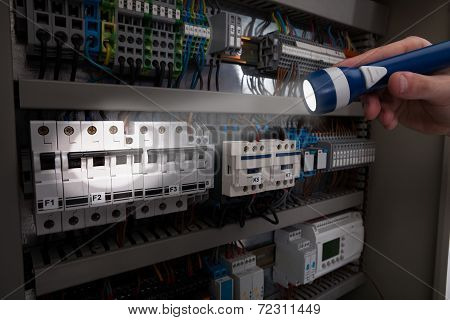 Technician Analyzing Fusebox With Flashlight