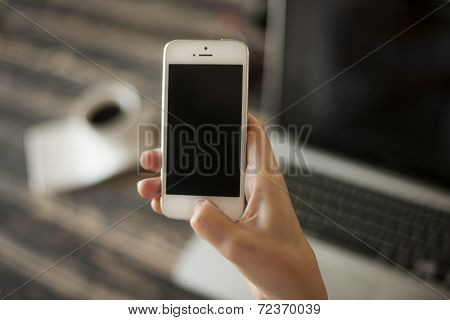 Woman Hand Holding Mobile Phone, And Laptop And Coffee Cup In Background