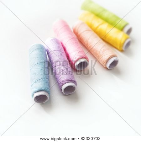 Spring colored thread spools. Light colored sewing threads on white table.