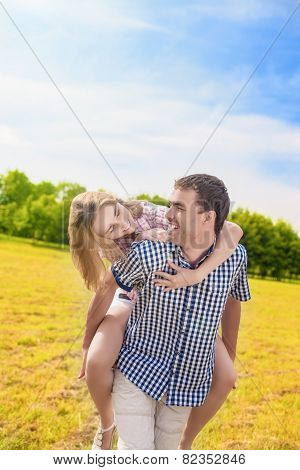 Happy Caucasian Couple Playing Outdoors In Summer. Having Fun While Piggybacking And Happiness Lifes