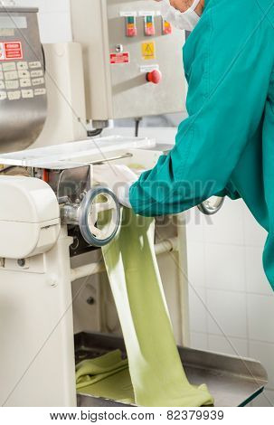 Midsection of chef processing spaghetti pasta sheet in machinery at commercial kitchen