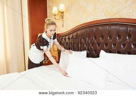 Hotel service. female housekeeping worker maid making bed with bedclothes at inn room