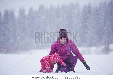 happy family on winter vacation, mom and cute little girl have fun and slide while snow falkes falling