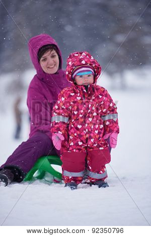 happy family on winter vacation, mom and cute little girl have fun and slide while snow falkes falling