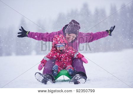 happy family on winter vacation, mom and cute little girl have fun and slide while snow falkes falling
