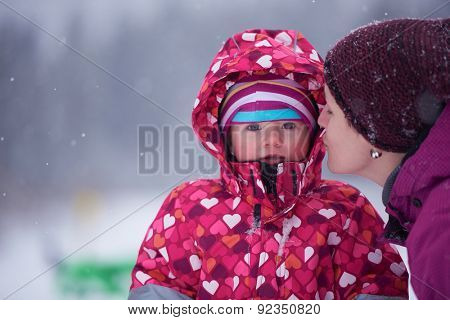 happy family on winter vacation, mom and cute little girl have fun and slide while snow falkes falling