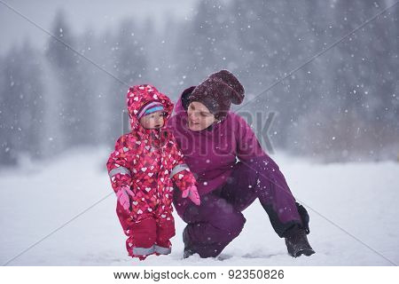 happy family on winter vacation, mom and cute little girl have fun and slide while snow falkes falling
