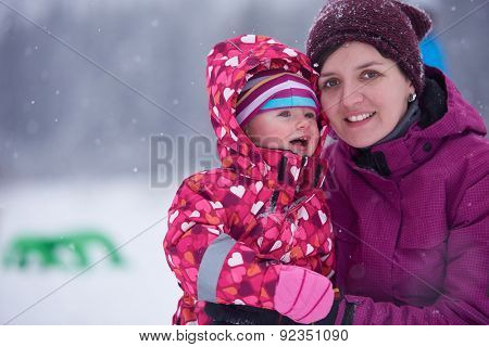 happy family on winter vacation, mom and cute little girl have fun and slide while snow falkes falling