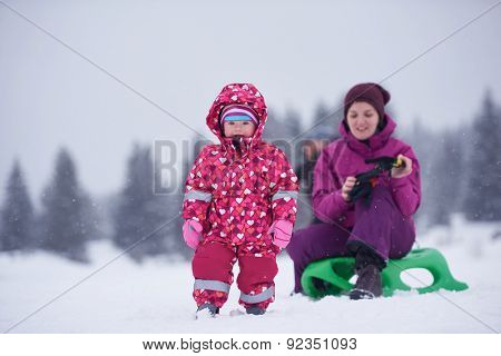 happy family on winter vacation, mom and cute little girl have fun and slide while snow falkes falling