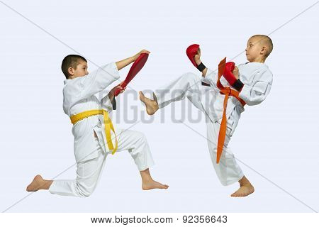 The sportsman with the orange belt beats kick on simulator in the hands of another athlete