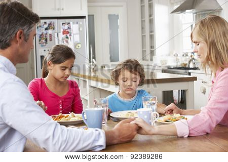 Family Praying Before Having Meal In Kitchen Together