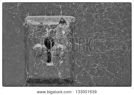 Cobwebs on a metal key hole of a wooden door. Black and white photo with a vintage border