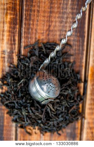 Vintage strainer with dry leaves of black tea on wooden background. Tea concept. Tea leaves. Top view. Closeup