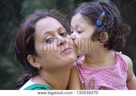 Daughter kissing her mother on cheek. Outdoors.  Mother's day, family, childhood and people concept.