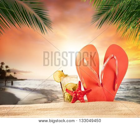 Tropical beach with drink and accessories in beautiful sunset with palm leaves on foreground. Copyspace for text