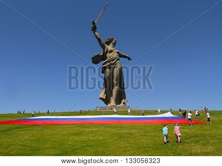 VOLGOGRAD RUSSIA - JUNE 12 2013: Boy and girl go to the aid of activists unfolding a large Russian flag in Day of Russia at the foot of the monument of Motherland Calls on Mamaev hill in Volgograd