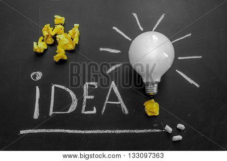 Light bulb with rays on the black chalkboard with title idea! written by white chalk and crumpled yellow papers light bulb idea business idea business concept Innovation concept