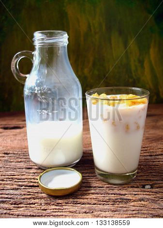 bottle of milk with corn cereals in glass on wooden
