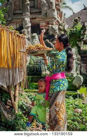 UBUD, INDONESIA - MARCH 01: Balinese woman with little son making offerings in the temple Ubud Bali Indonesia on March 01 2016