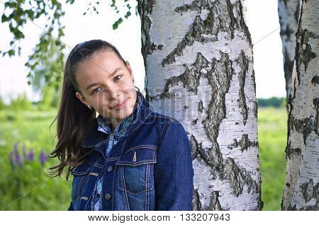 Girl standing near birch tree in summer tilting her head and smiling