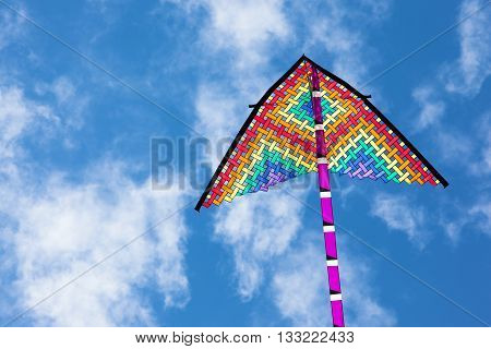 Rainbow colored kite flying high against sunny blue skies for Summer and vacation concept.