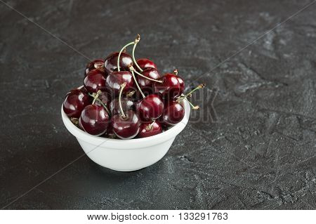 Ripe cherry berries in white plate on concrete background
