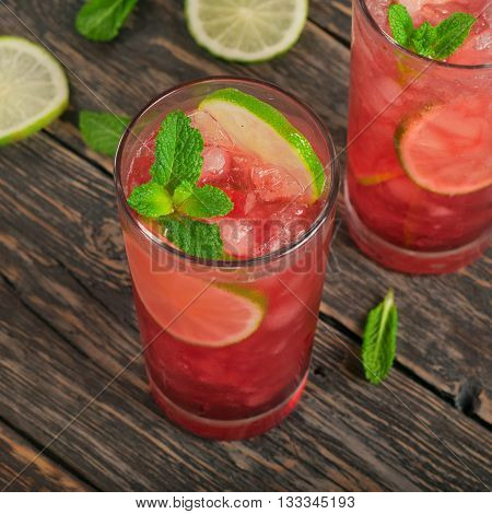 Two red cocktail with ice lime and mint in tall glass on dark wooden background. Top view with copy space