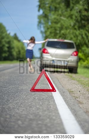 Red triangle warning sign and woman calling for assistance after breakdown of her car. Focus on triangle.
