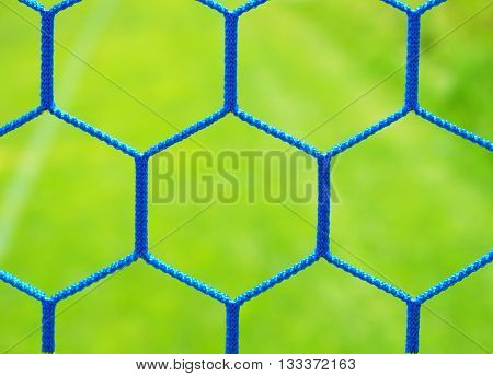Detail of yellow blue crossed soccer nets, soccer football in goal net with grass on playground in background. Honeycomb shape.