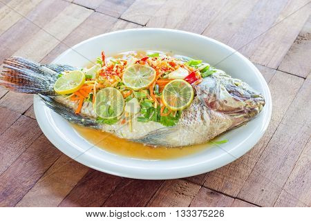 steamed Nilotica fishthai style steamed fish in spicy saucewood background