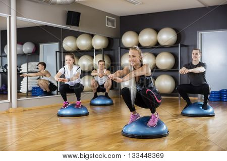 Friends Doing Squatting Exercise On Bosu Ball In Gym