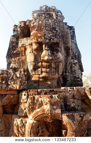 Dramatic view at sunset of one of the many large stone carved faces of Bayon Temple in Angkor Thom Angkor district Siem Reap Cambodia